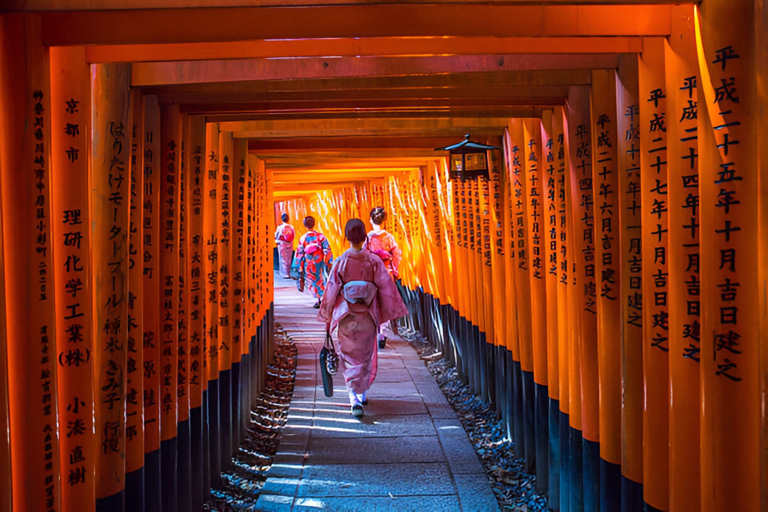 Women in kimonos walking through Fushimi Inari Shrine torii gates Kyoto Japan
